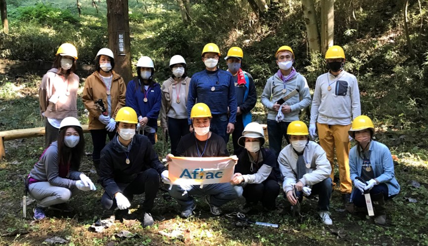 A group of Aflac employees posing with an Aflac banner in the woods